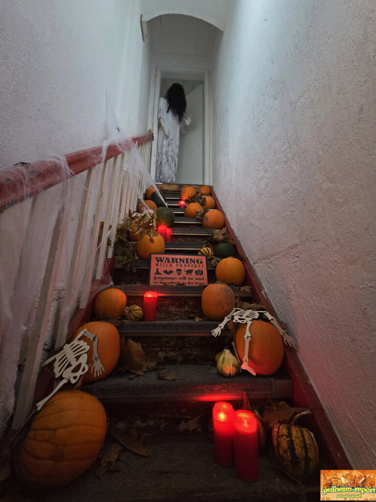 Eine schaurige Gestalt auf einer Treppe voller Kürbisse, Kerzen und Skelette
